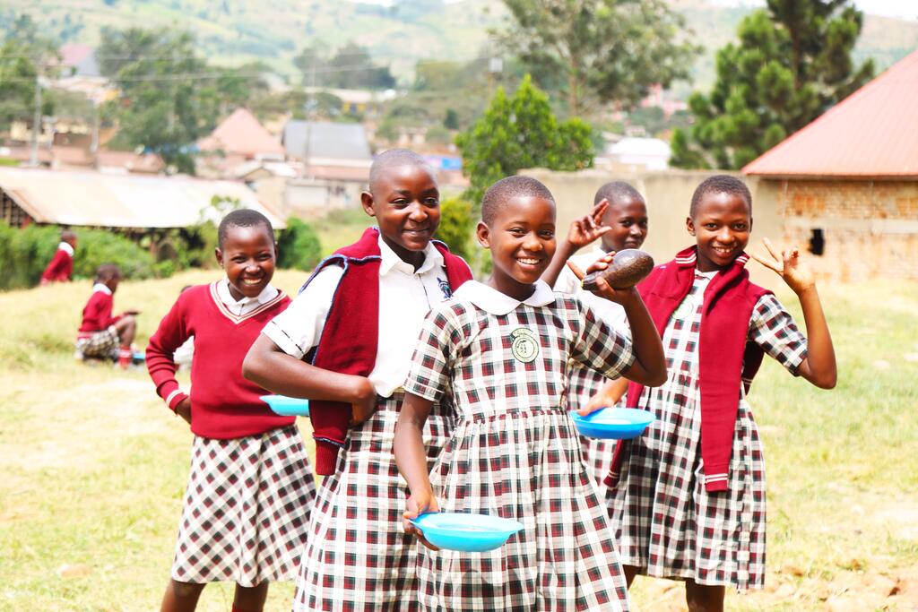 Four pupils in school uniform holding bowls, with their village behind them